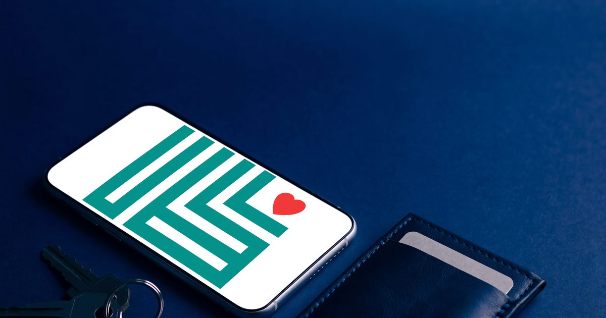 A smartphone showing a simple QR-style pattern with a small red heart, next to a wallet and keys on a navy surface.