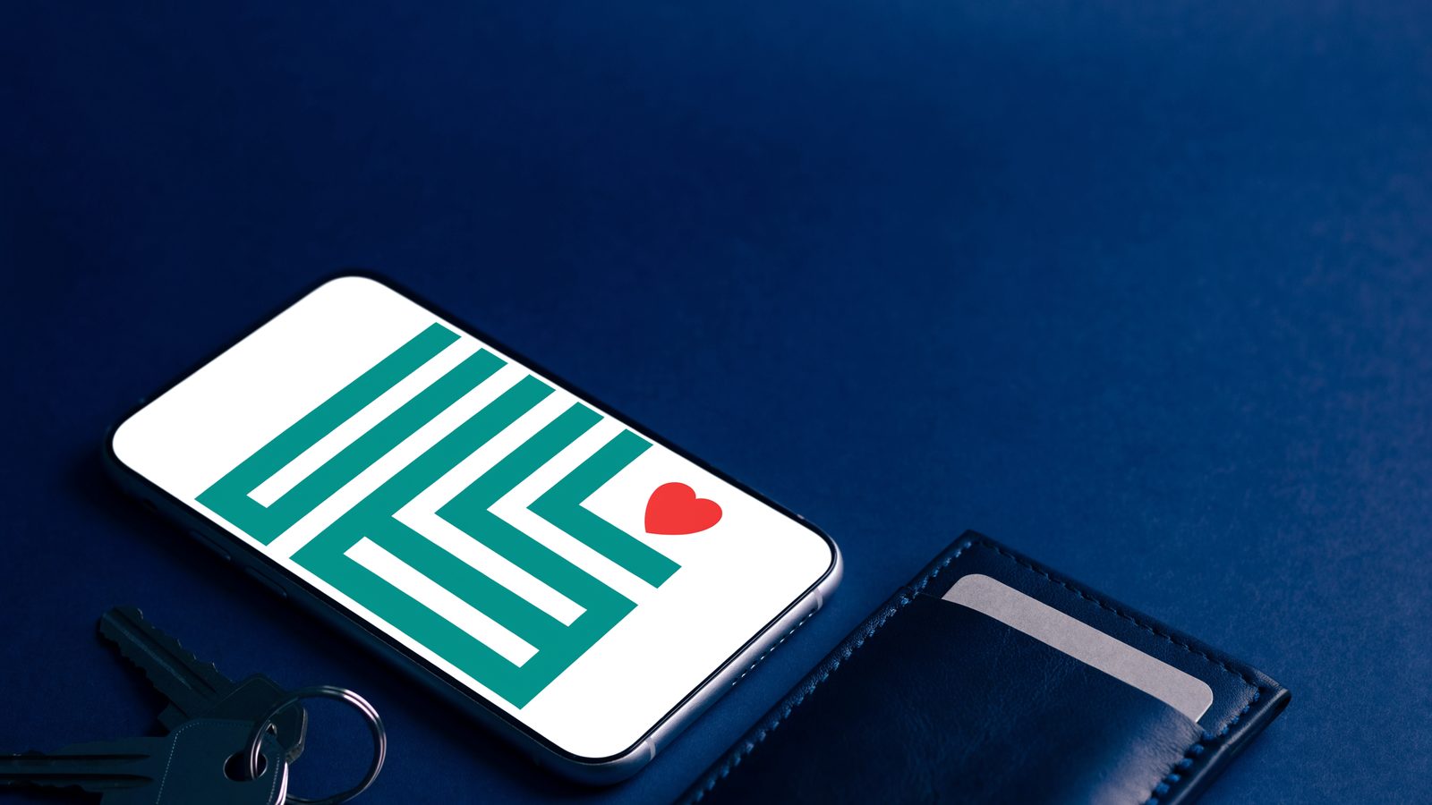 A smartphone showing a simple QR-style pattern with a small red heart, next to a wallet and keys on a navy surface.